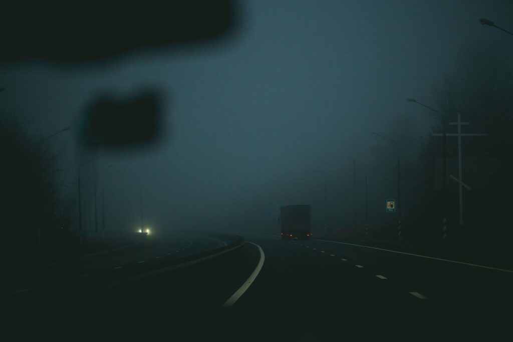 A dull, foggy road with two cars driving down it
